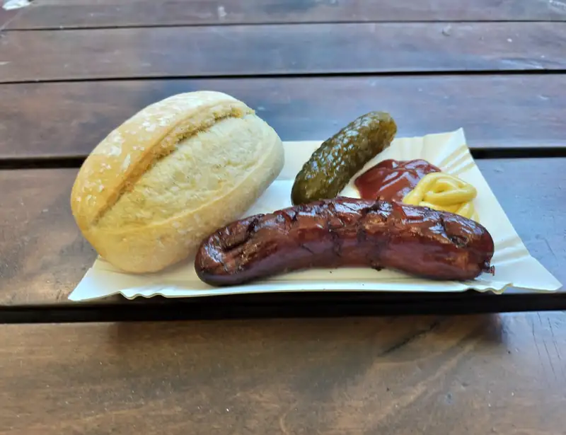 Kiełbasa z grilla z bułką i ogórkiem na drewnianym stole